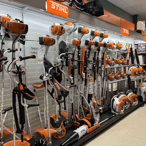 A store display features various orange and white STIHL garden tools, including trimmers and leaf blowers. The well-organized arrangement suggests a focus on order and efficiency.