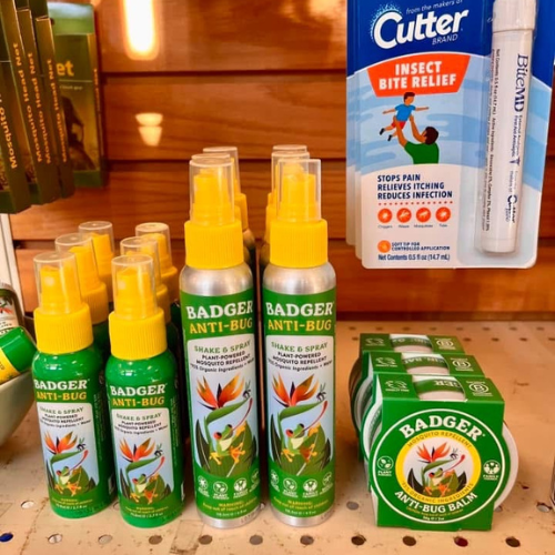 Shelves display green Badger Anti-Bug spray bottles with yellow caps, Badger Anti-Bug balm in green tins, and a Cutter insect bite relief pen.