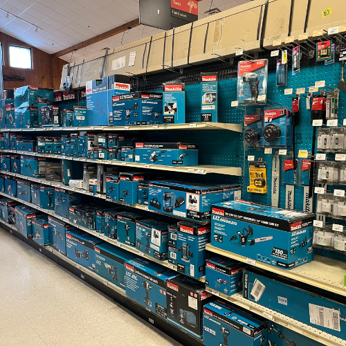 A hardware store aisle displays a variety of power tools and accessories in blue boxes on shelves. Bright lighting and organized layout create an inviting shopping atmosphere.
