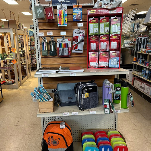 A store display featuring office and school supplies, including binders, backpacks, pens, and highlighters, arranged neatly on shelves. The atmosphere is organized and inviting.