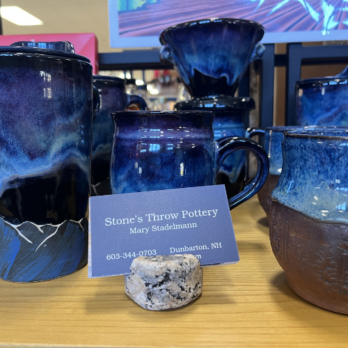 Ceramic pottery display features vibrant blue and brown pottery with a marbled texture. A business card in front reads 