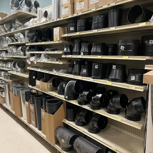 Shelves filled with a variety of black metal duct fittings and connectors in a hardware store. Products are neatly organized for easy selection.