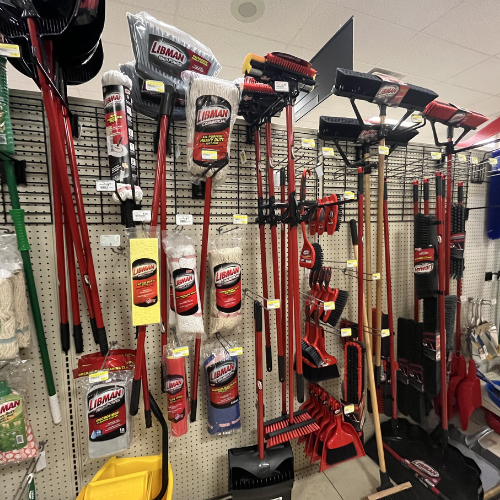 A store display showcasing red and black rakes, brooms, and shovels hangs neatly on a pegboard wall, evoking a sense of organization and readiness.