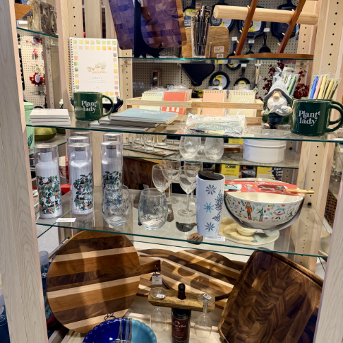Store display featuring kitchenware and decor. Shelves hold wooden boards, glassware, mugs with 