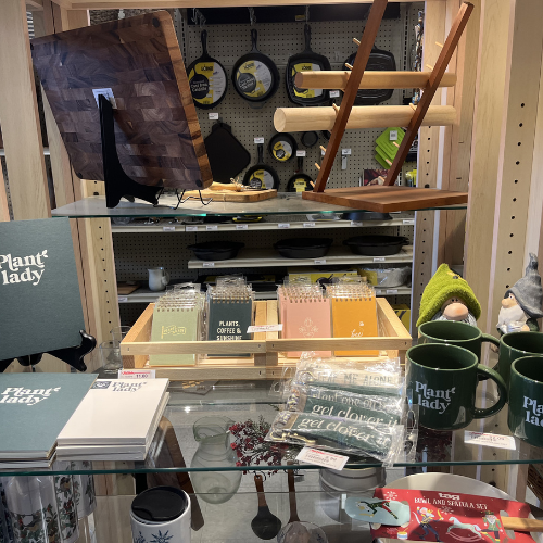 A wooden shelf displays kitchenware like cutting boards, mugs labeled 