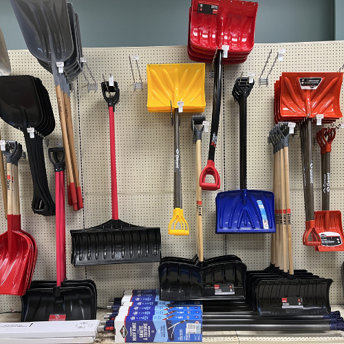 A display of colorful snow shovels in red, yellow, blue, and black, neatly arranged on a pegboard in a hardware store, creating a vibrant, organized look.