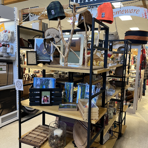 A store display shelf features rustic decor, including photo frames, a wooden branch centerpiece, hats, and candles. The ambiance is cozy and inviting.
