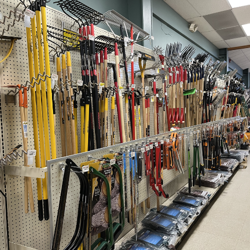 A hardware store aisle displays a variety of gardening tools like rakes, shovels, and shears. Items are organized neatly on a pegboard, evoking a sense of order.