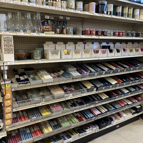 Store shelf filled with colorful candles and glass holders. Candles are neatly organized by shade, creating a vibrant, inviting display.