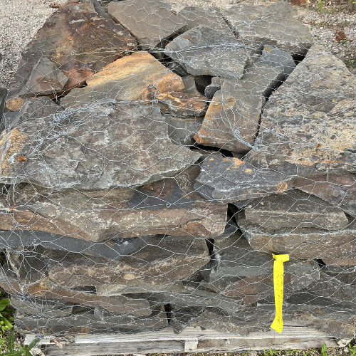 A stack of irregular, weathered gray stones secured with wire mesh on a wooden pallet. A yellow tag is attached, suggesting industrial use.