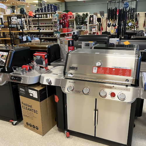 A store display featuring stainless steel grills, accessories, and tool racks. Bright, organized setting conveying a sense of readiness for outdoor cooking.